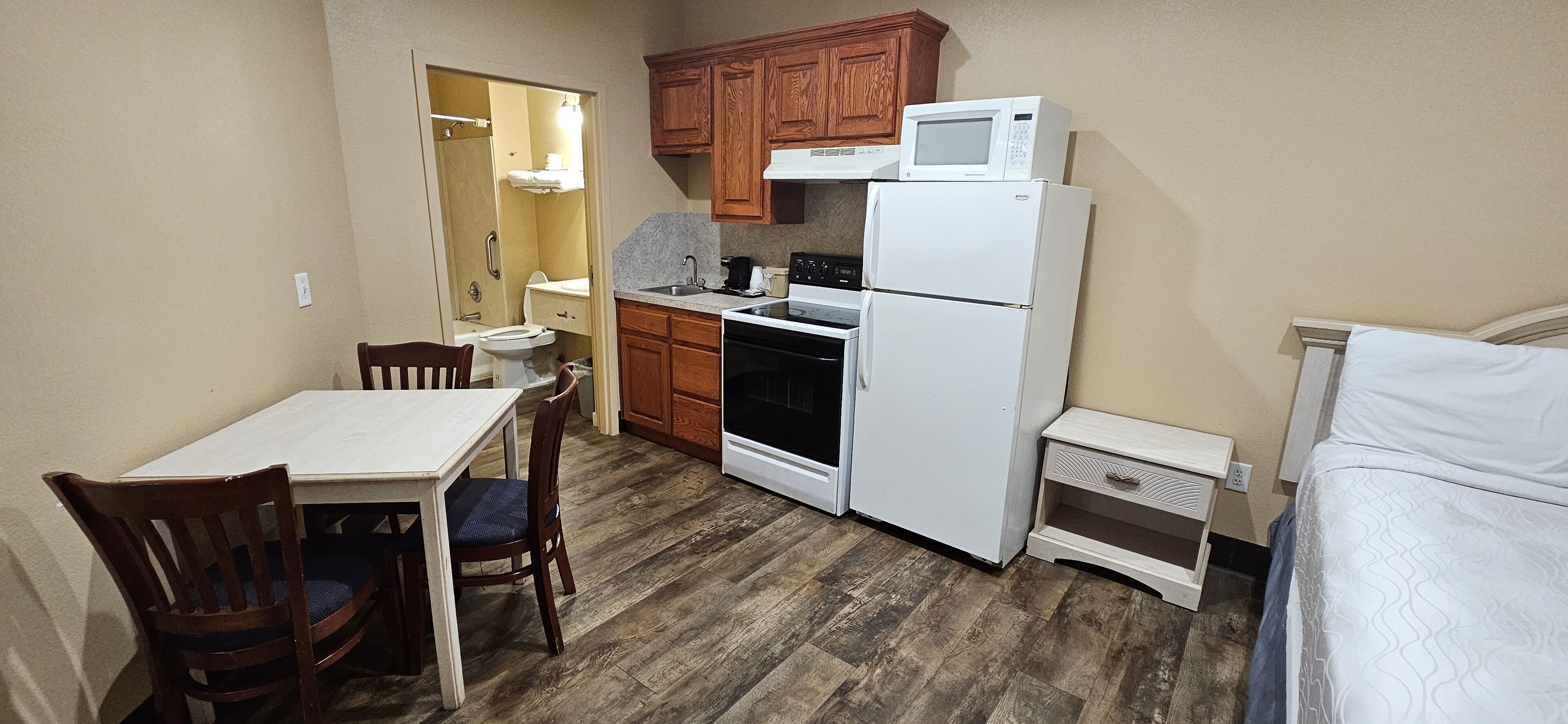 A compact kitchen with wooden cabinets, a white refrigerator, a microwave, a stove, and a dining area with a table and chairs.