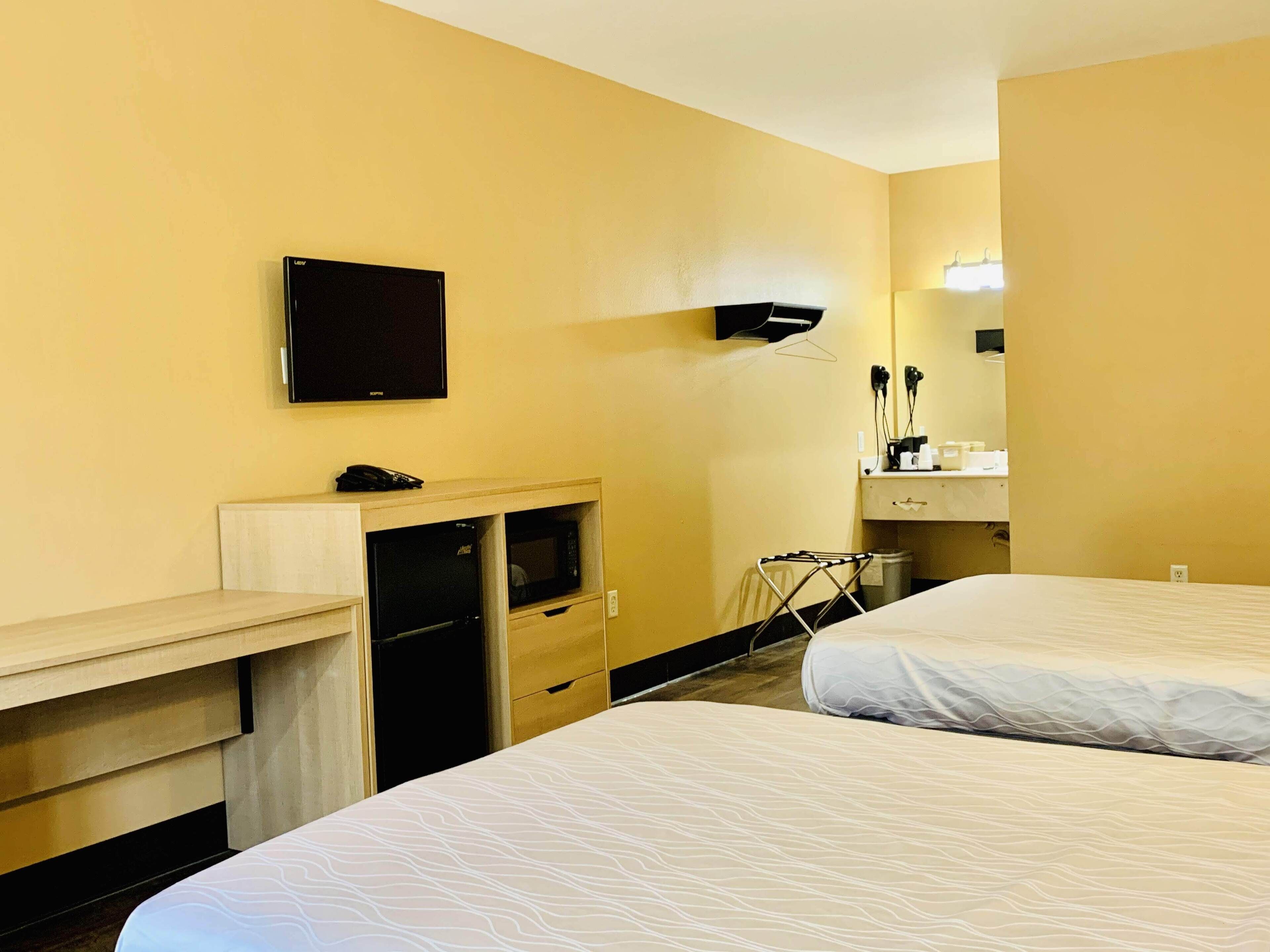 Een hotelkamer met twee bedden, een bureau met een magnetron, een televisie en een spiegel.