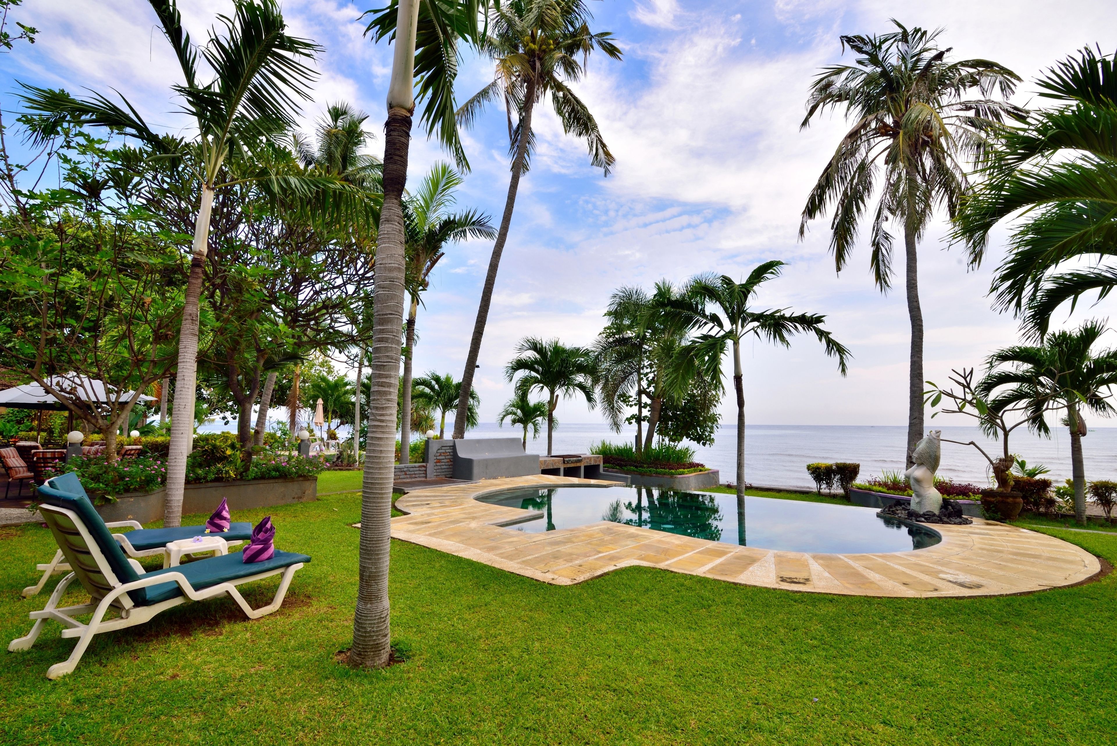 A pool area with lounge chairs, palm trees, and a view of the ocean.