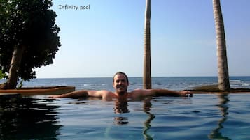 Un hombre en una piscina infinita con vistas al océano y palmeras.