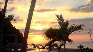 A sunset view from a beachside location with palm trees and a thatched-roof structure. - Dolphin Beach Bali (Banjar)