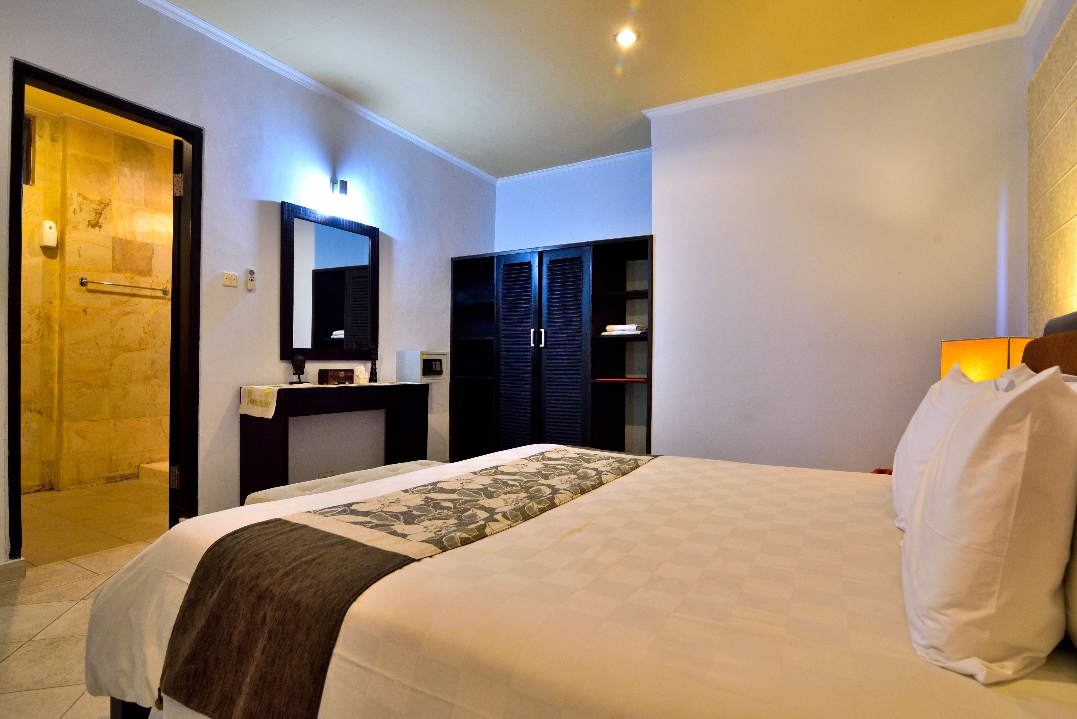 Habitación de hotel con una cama grande, una mesita de noche, un espejo, un armario y la puerta del baño.