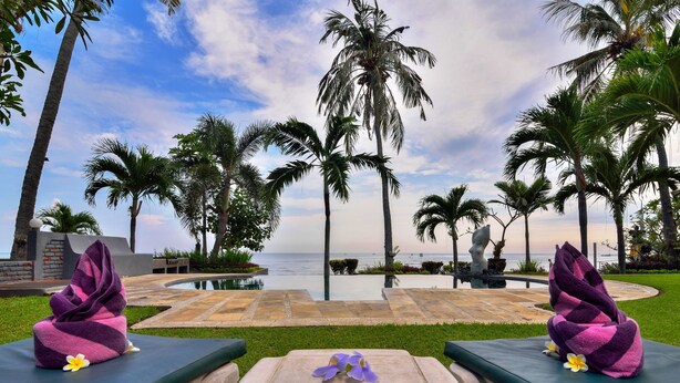 A poolside lounge with two cushioned chairs, a small table, and a view of the ocean. - Dolphin Beach Bali (Banjar)