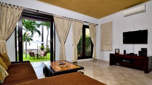 A living room with a sofa, a coffee table, a TV, and a sliding glass door leading to a patio with outdoor furniture. - Dolphin Beach Bali (Banjar)