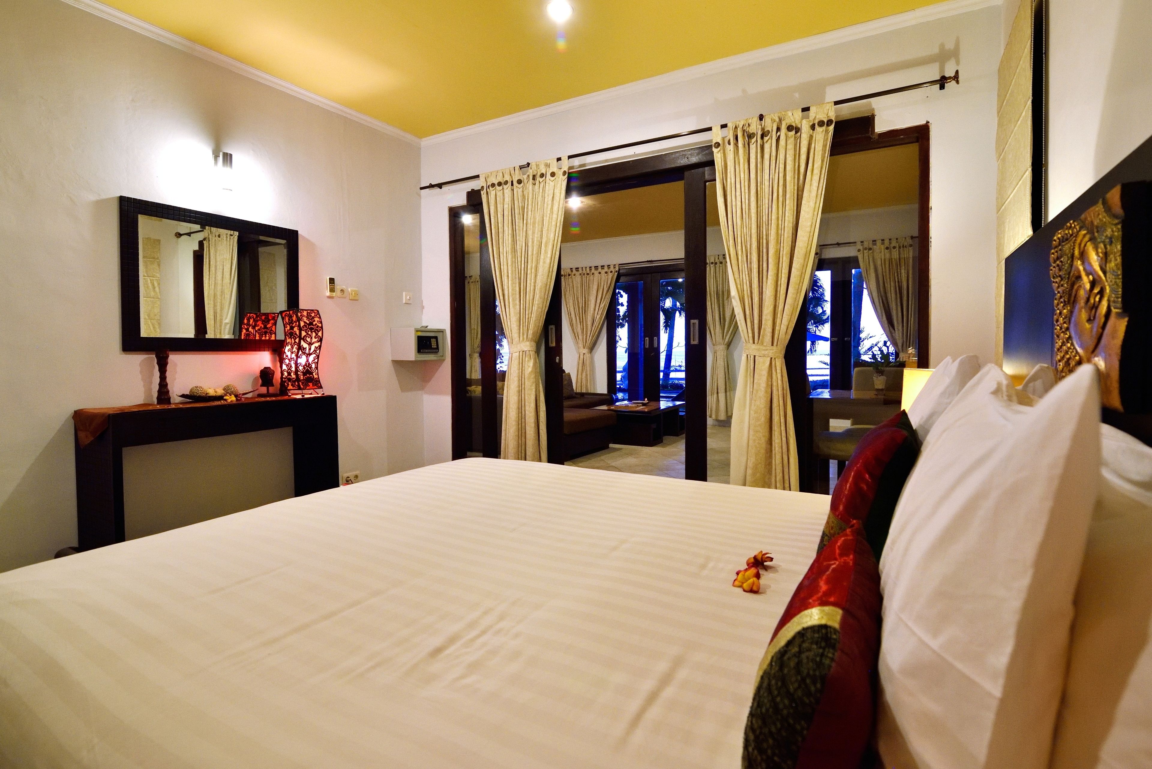 A hotel room with a large bed, a bedside table with a lamp, a mirror, and curtains.