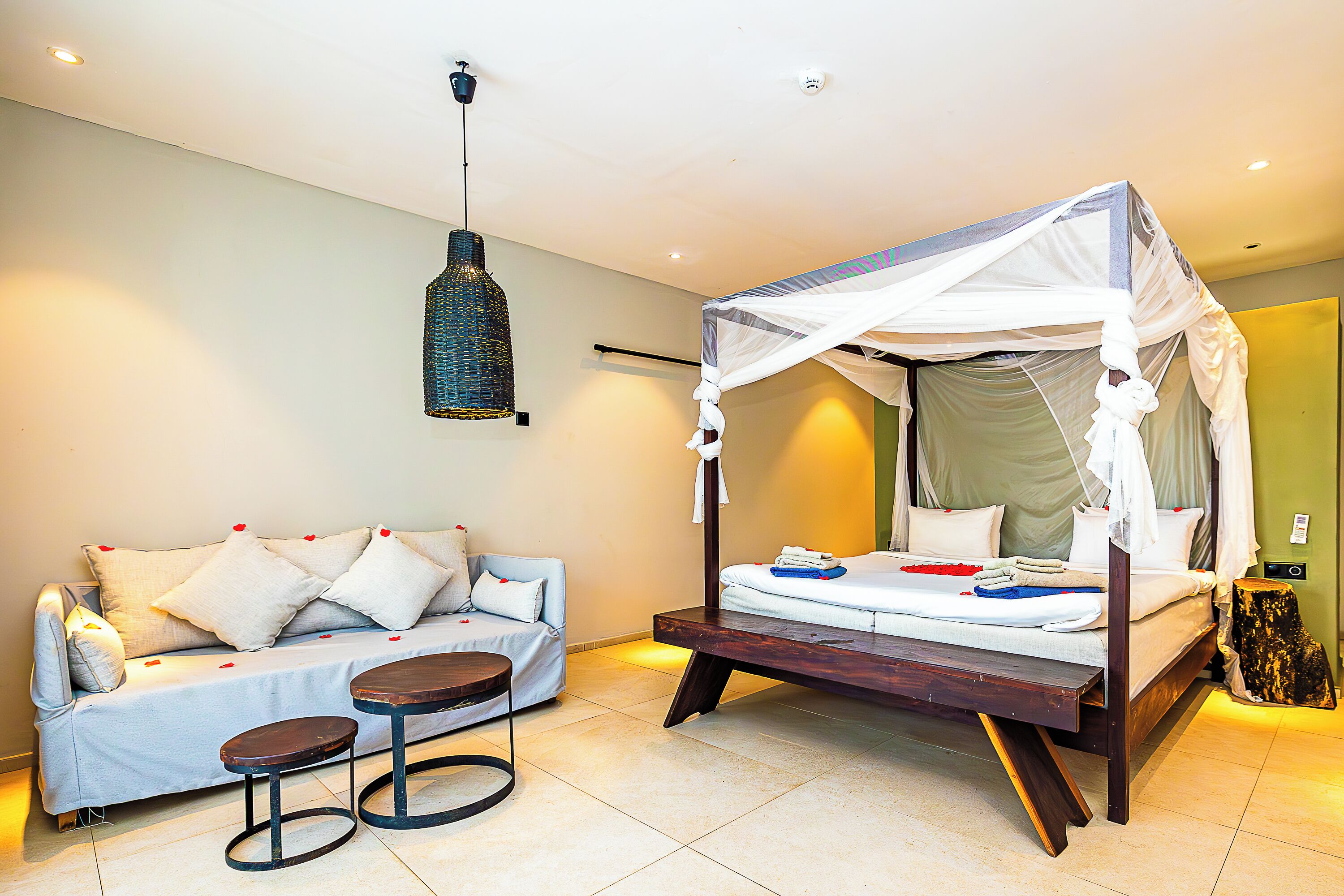 A bedroom with a bed, a sofa, a small table, and a hanging light fixture.