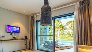 A hotel room with a TV, a desk, a bed, a window with a view of a pool and palm trees.