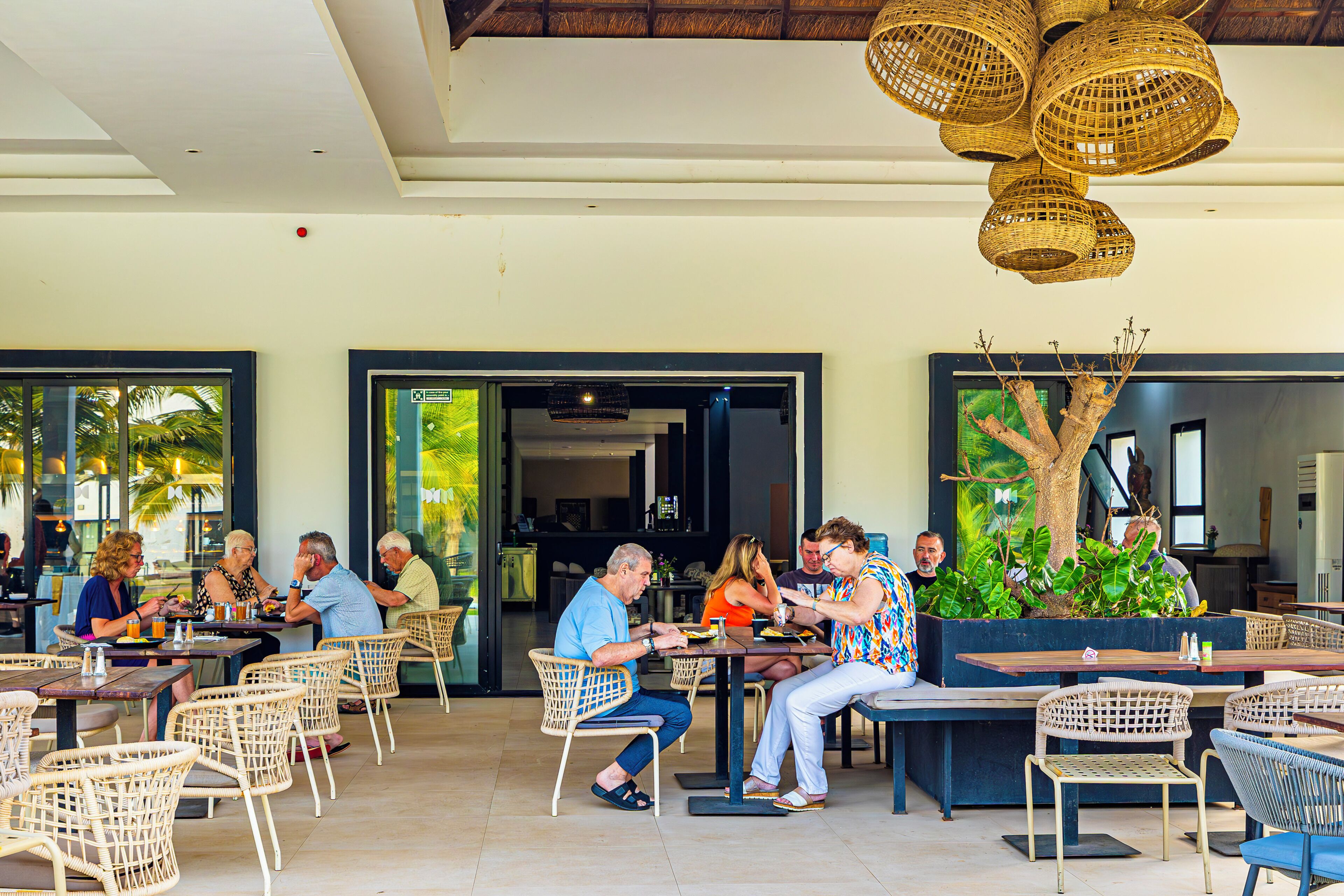 An outdoor dining area with wicker furniture, a tree planter, and a ceiling with woven light fixtures.