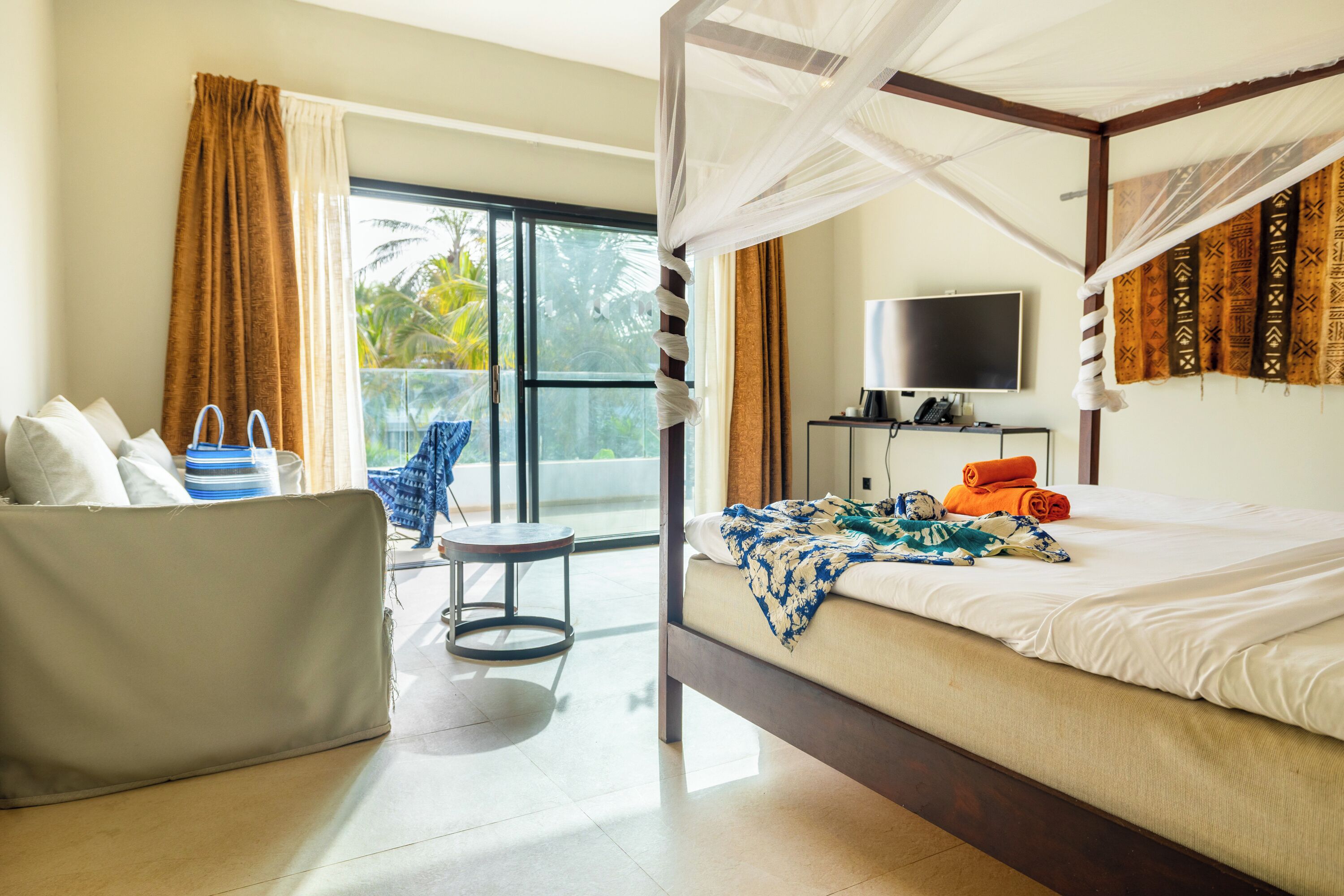 A room with a bed, a chair, a TV, and a balcony with curtains.