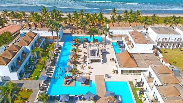 A resort with a central swimming pool, multiple lounge areas, and a beach view.