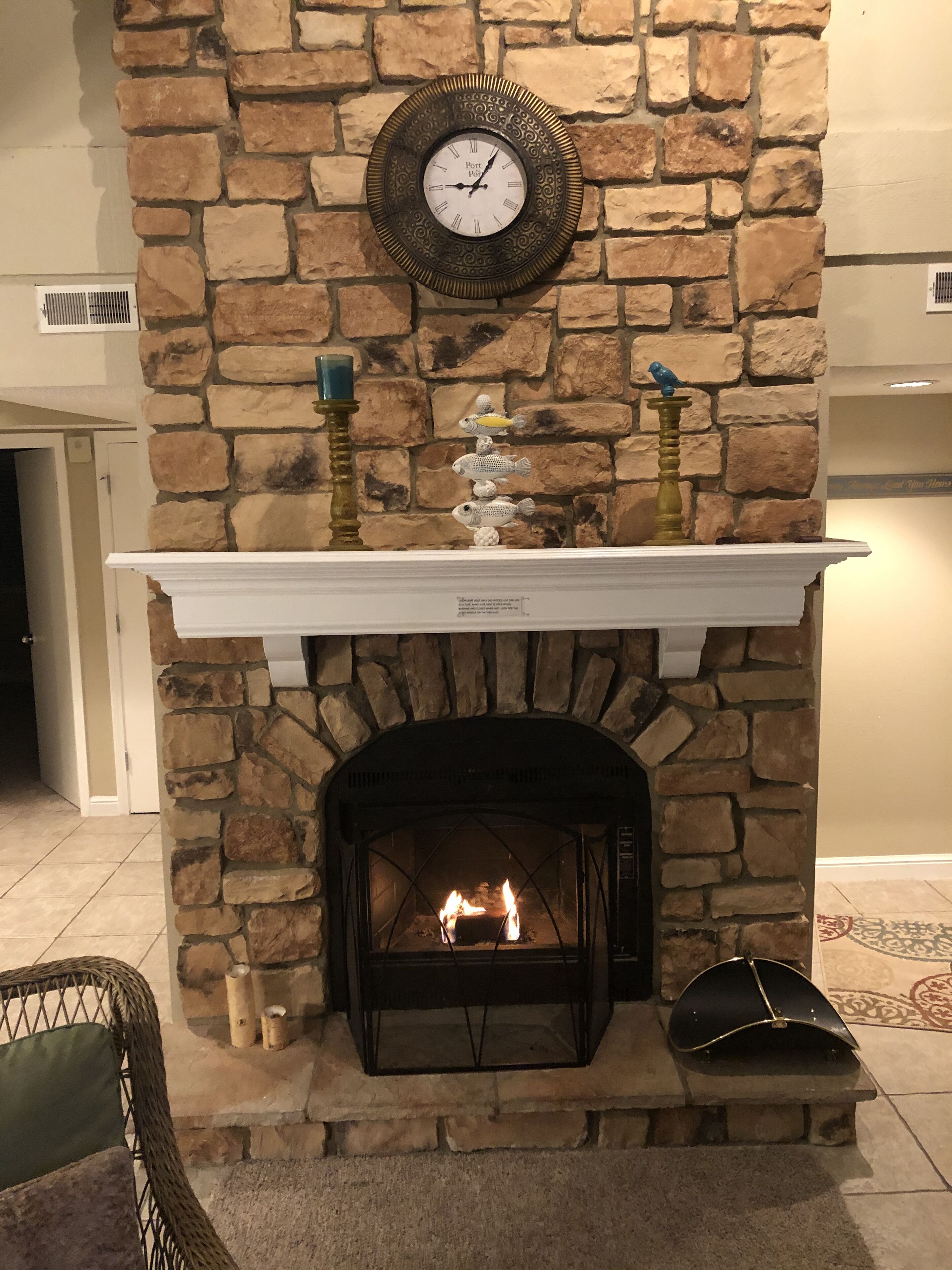 A stone fireplace with a clock above it, a mantel with decorative items, and a fire burning inside.