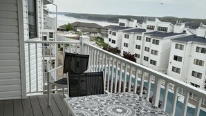 Uma varanda com mesa e cadeiras estampadas, com vista para uma área residencial com vários edifícios e um corpo de água ao fundo.