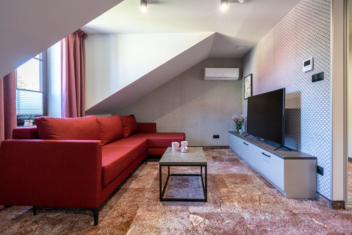 A modern living room with a red sofa, a coffee table, and a TV on a white cabinet.