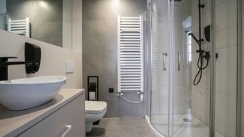 Un baño moderno con lavamanos blanco, inodoro y zona de ducha con mampara de vidrio.