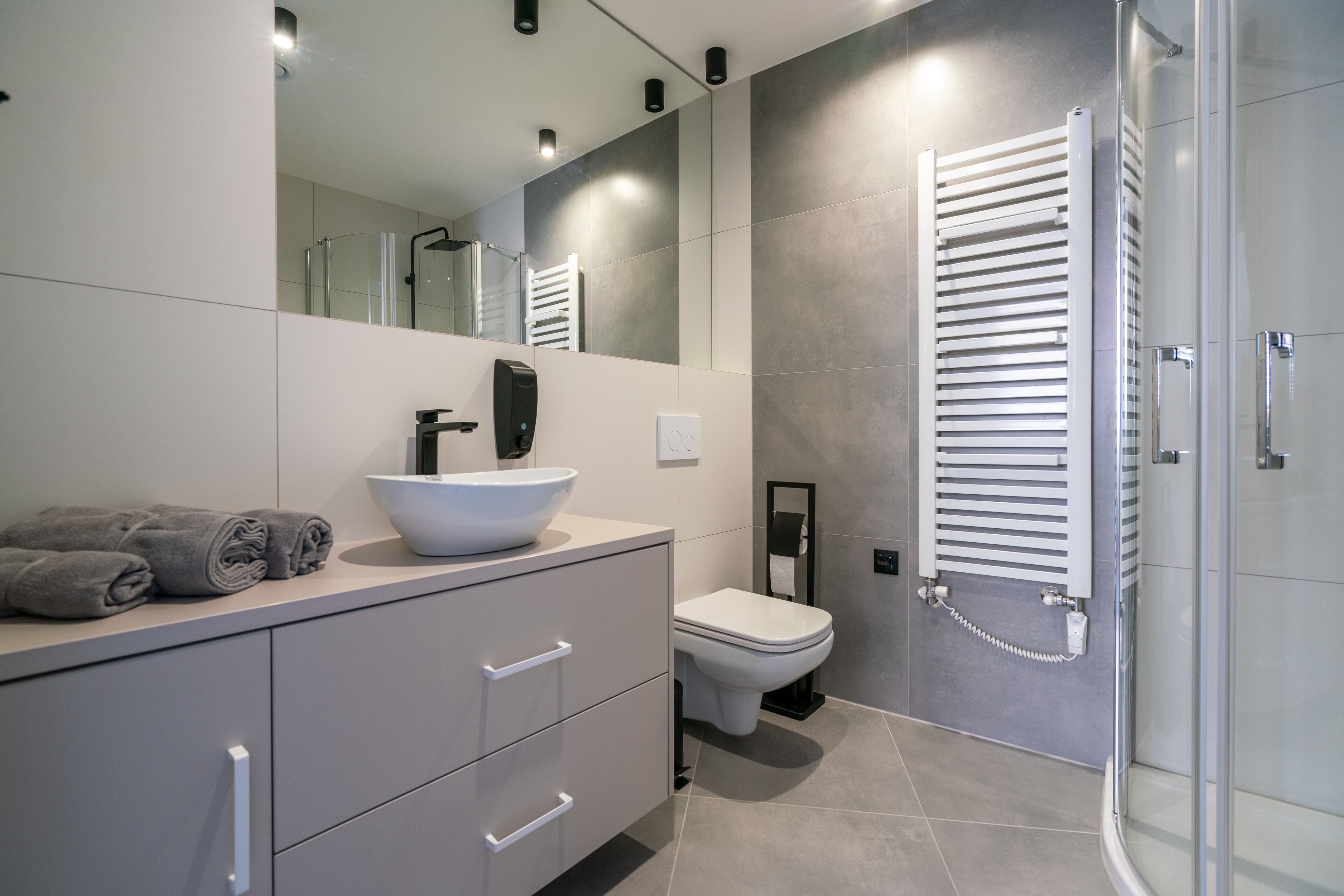 Une salle de bain moderne avec un meuble-lavabo blanc, un grand miroir, des toilettes blanches et une douche à parois de verre.