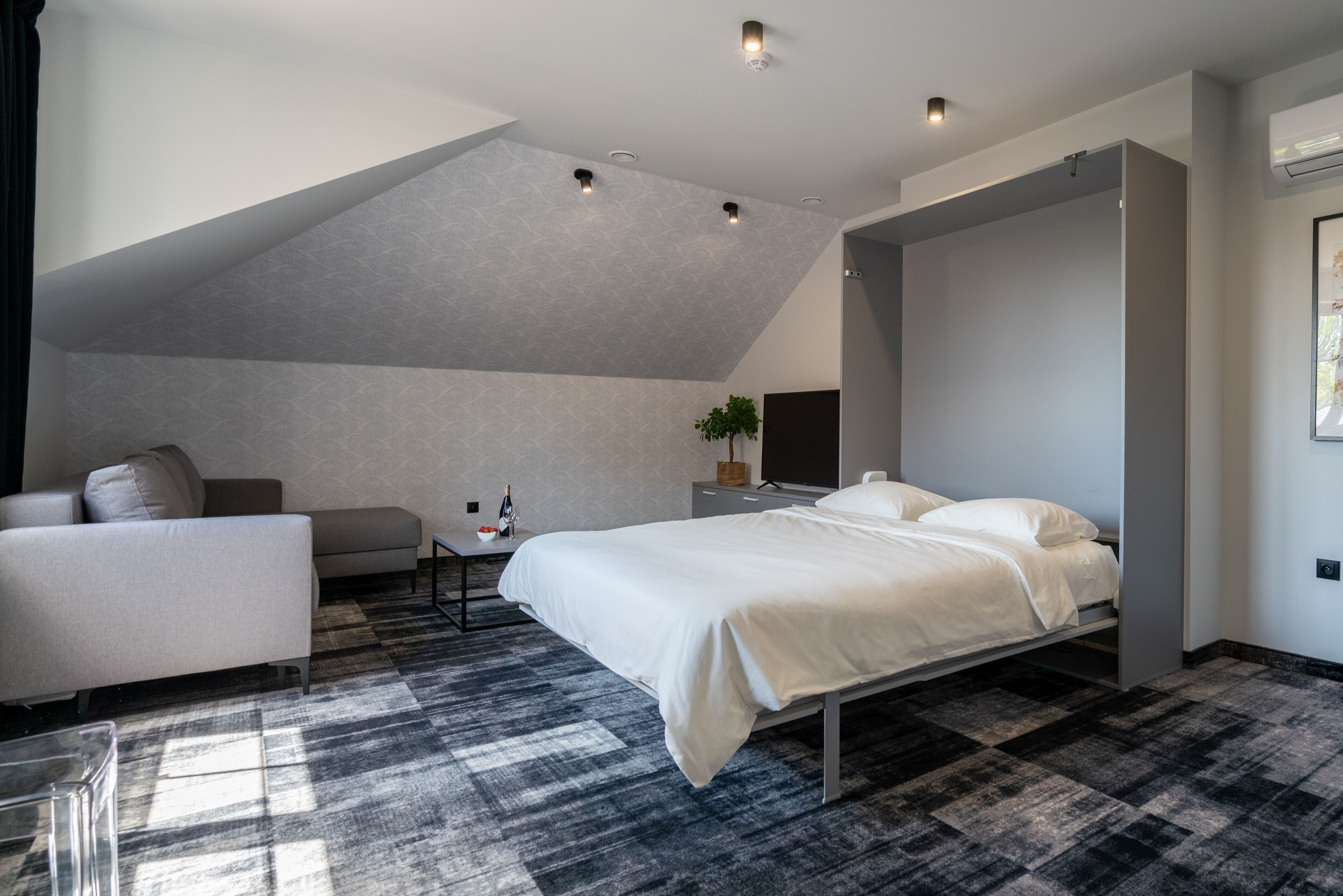 A modern bedroom with a sloped ceiling, a bed, a sofa, and a small table with a plant.