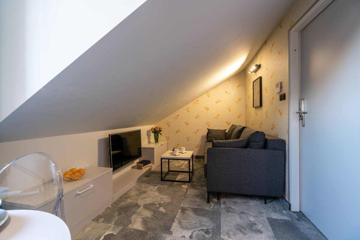 A small, modern room with a gray sofa, a flat-screen TV, a small table, and a white cabinet.