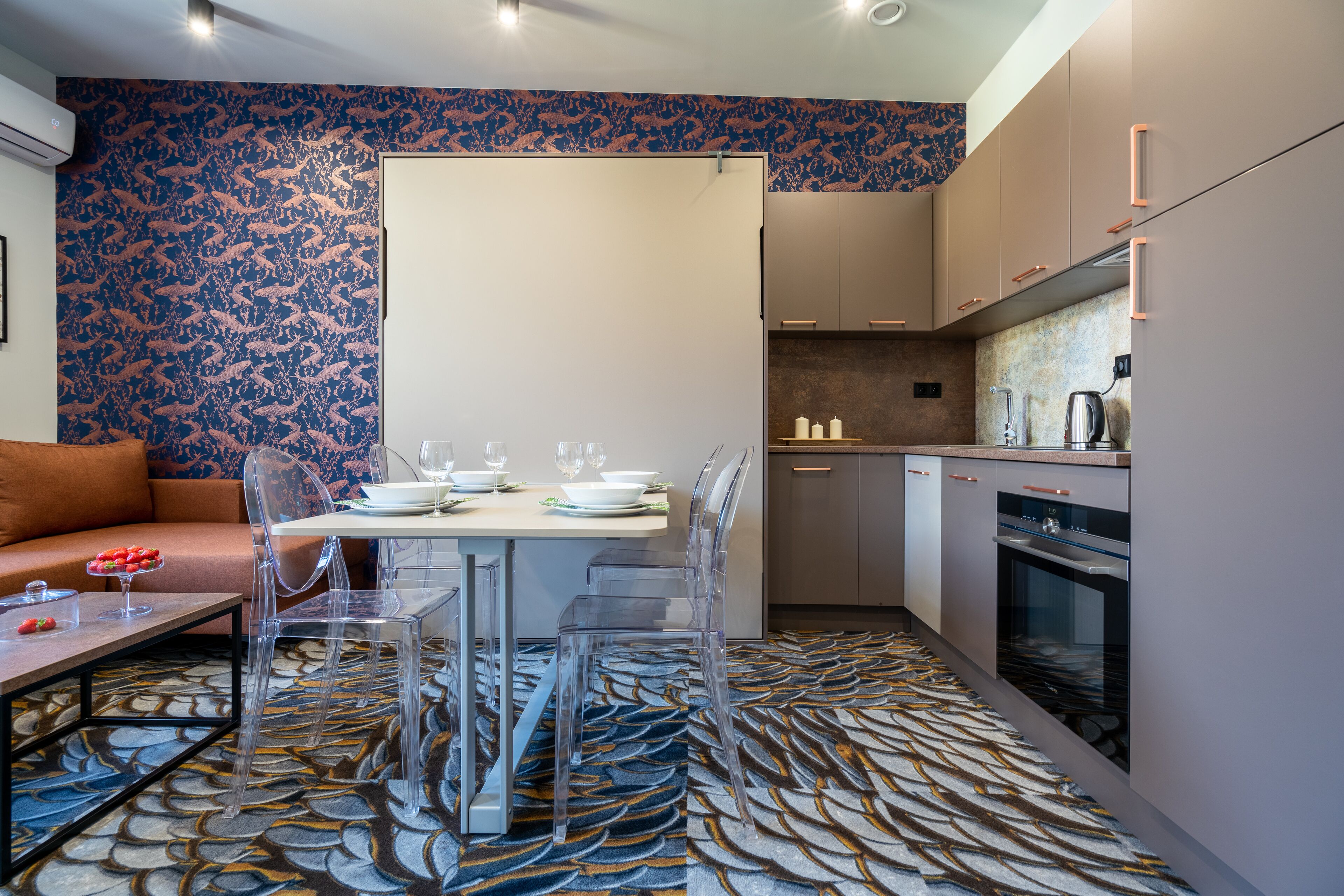 Una cocina moderna con comedor, que incluye una alfombra estampada, sillas traslúcidas y un sofá.