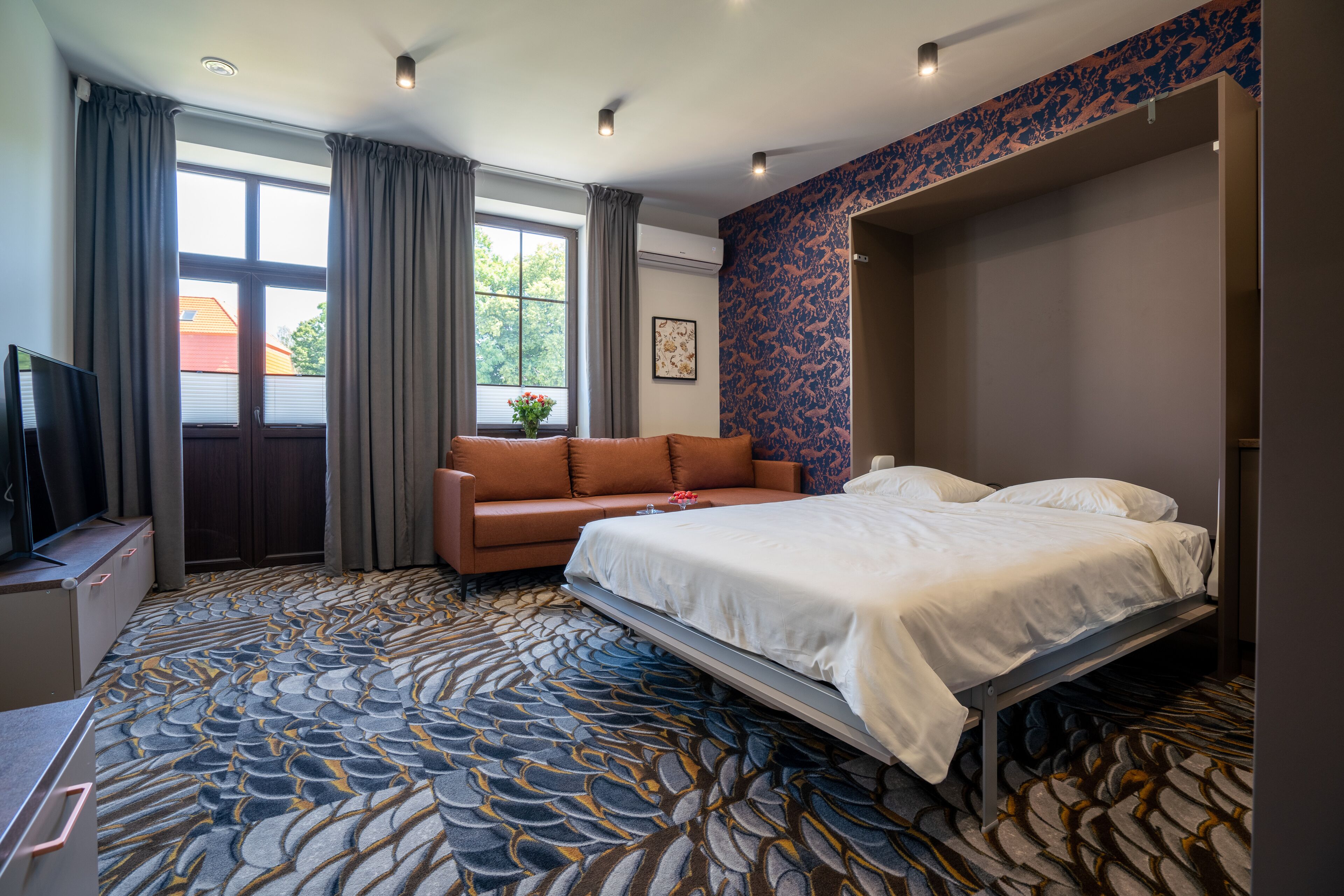 A hotel room with a bed, a sofa, a TV, and a window with curtains.