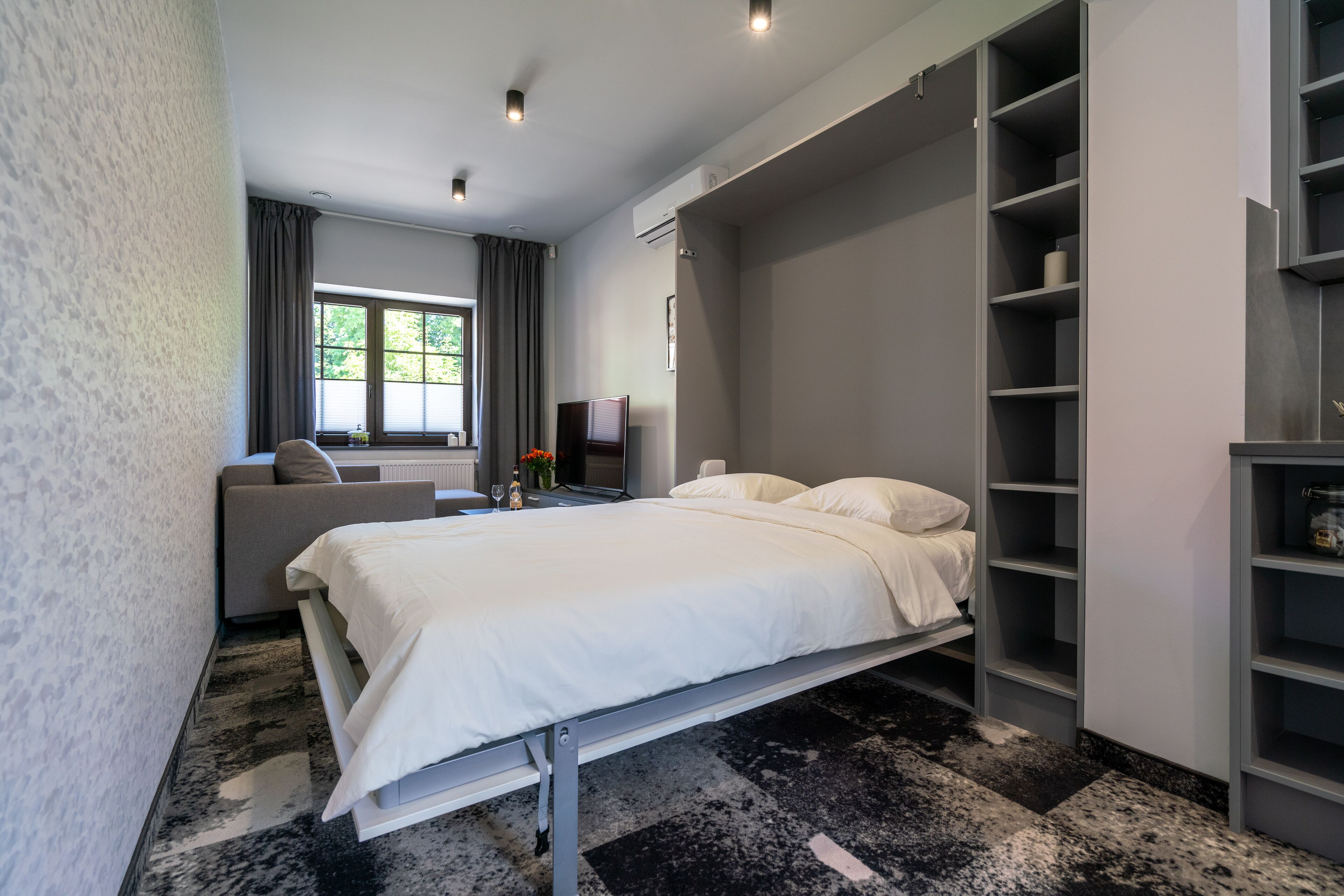 Una camera da letto moderna con un letto, una poltrona, una TV e una libreria a muro.