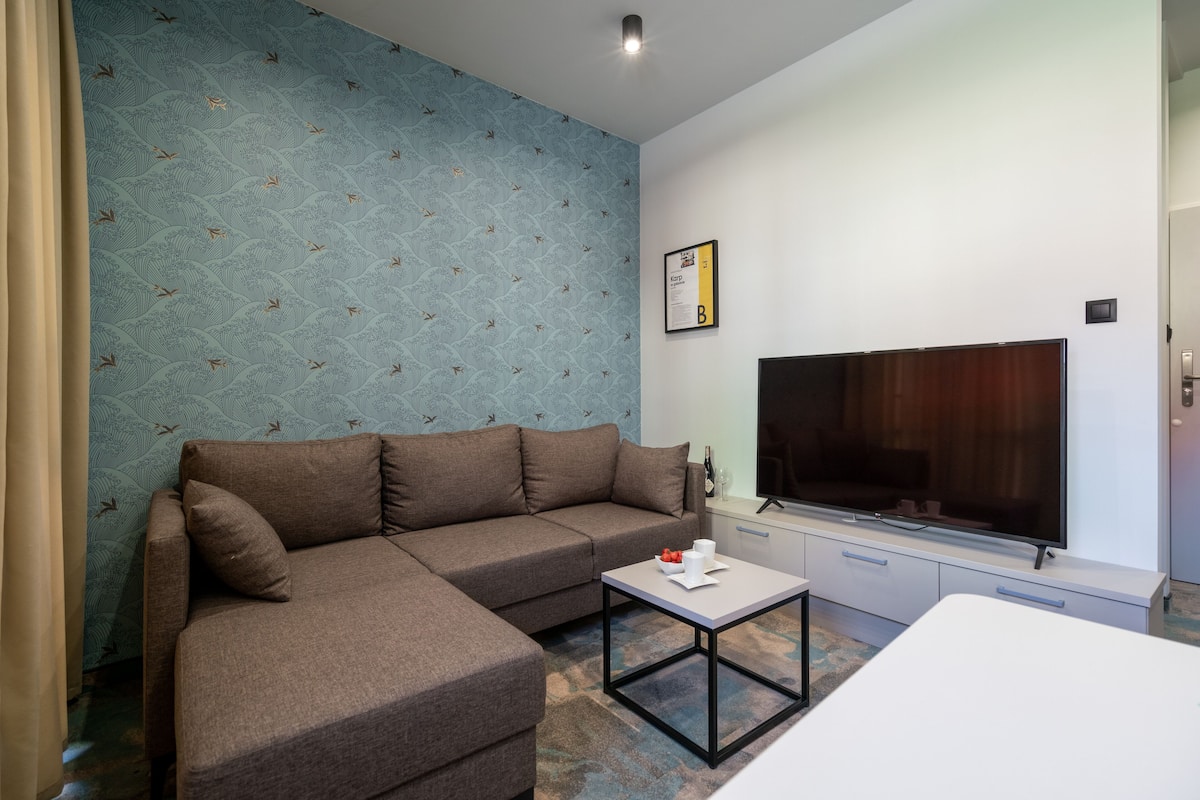 A modern living room with a sectional sofa, a flat-screen TV, a coffee table, and a small cabinet.