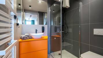 A modern bathroom with a glass shower enclosure, a white sink, and a wooden vanity.