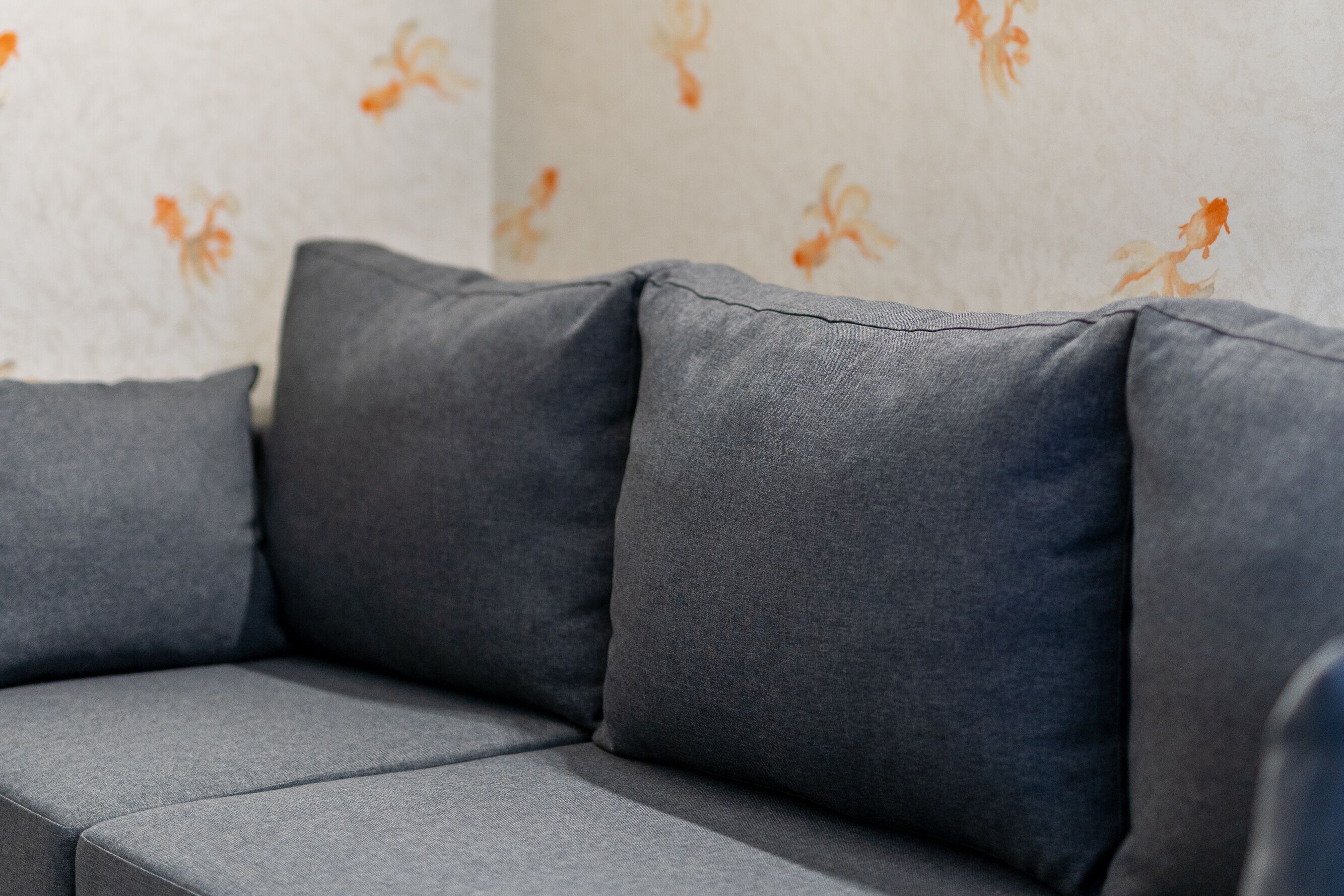 En grå sofa med blomstret tapet bag sig.