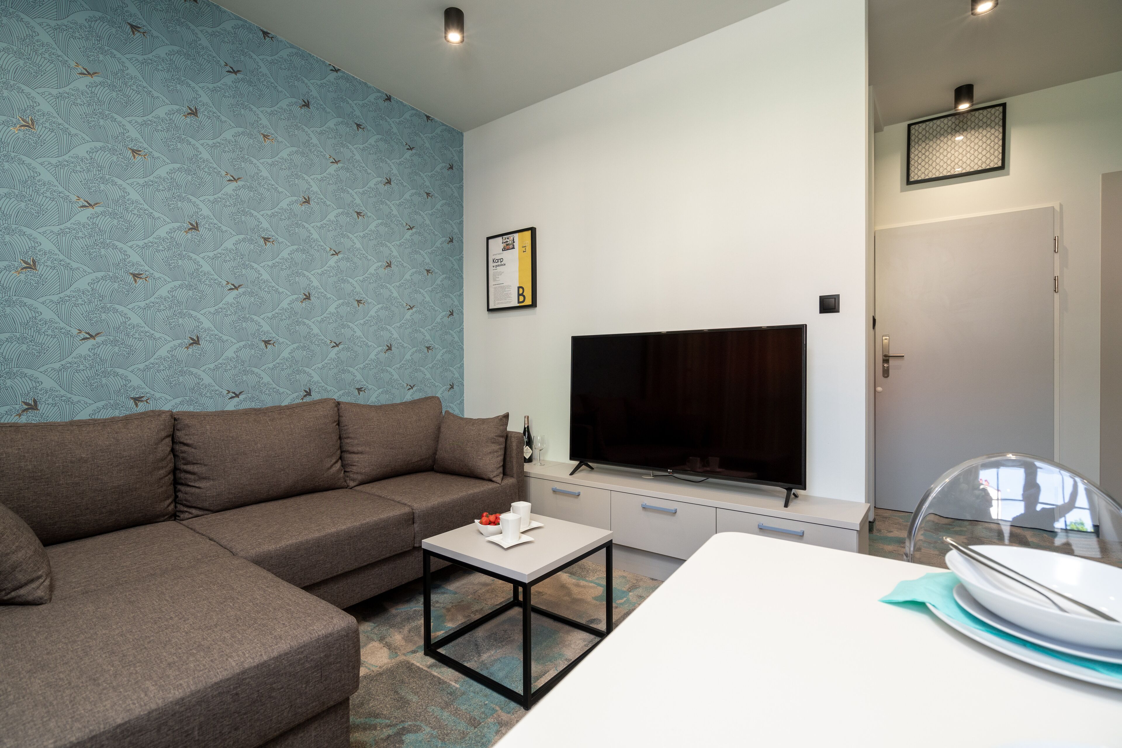 A modern living room with a sectional sofa, a flat-screen TV, a dining table, and a kitchen area.