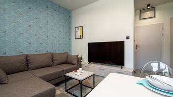 A modern living room with a sectional sofa, a flat-screen TV, a dining table, and a kitchen area.