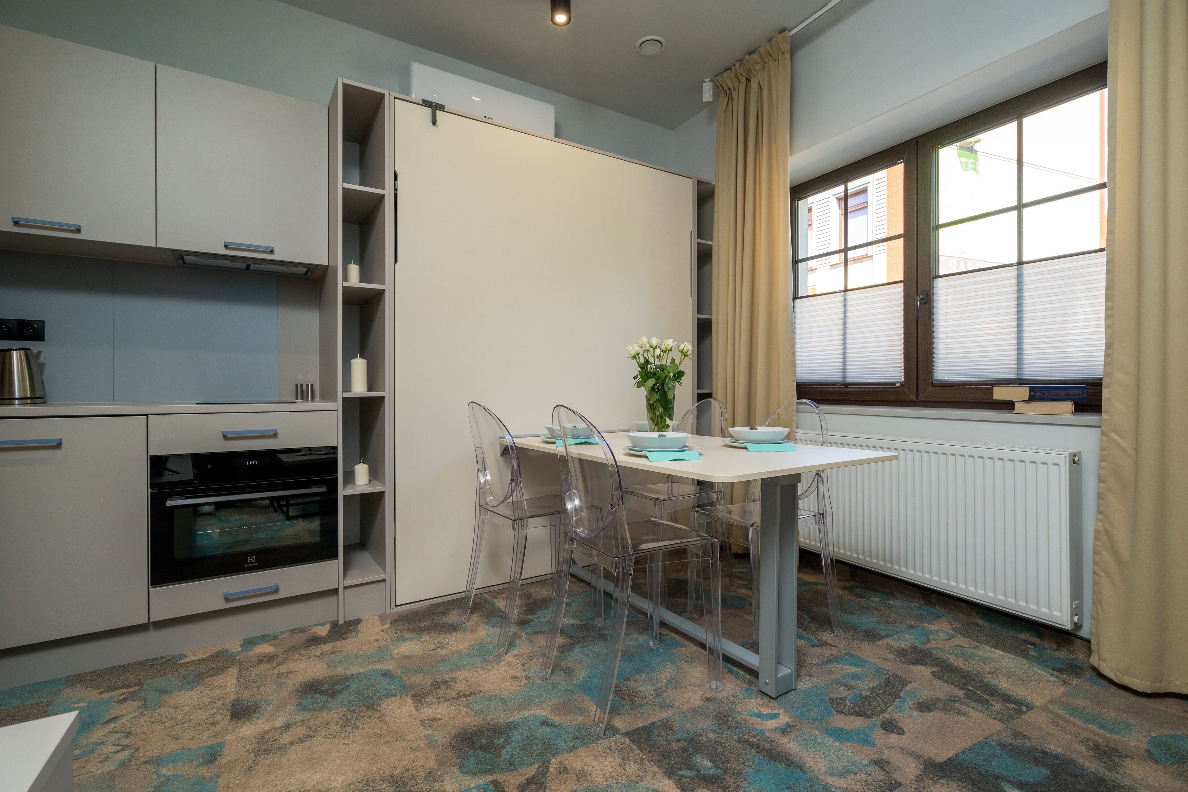 Una cocina moderna con horno empotrado, una mesa de comedor con sillas y un ventanal con cortinas.