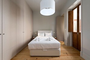 A modern bedroom with a large bed, wooden flooring, and a large window.