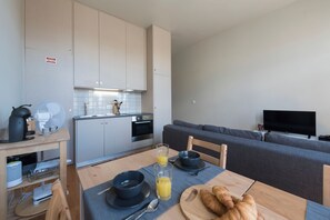A modern kitchen with a dining area, a grey sofa, and a flat-screen TV.