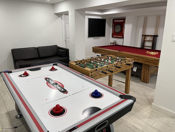 A room with a foosball table, a pool table, and a billiards table.
