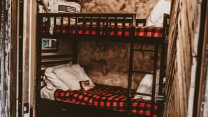 Een rustieke kamer met een stapelbed, een stoel en een bloemenkleed.