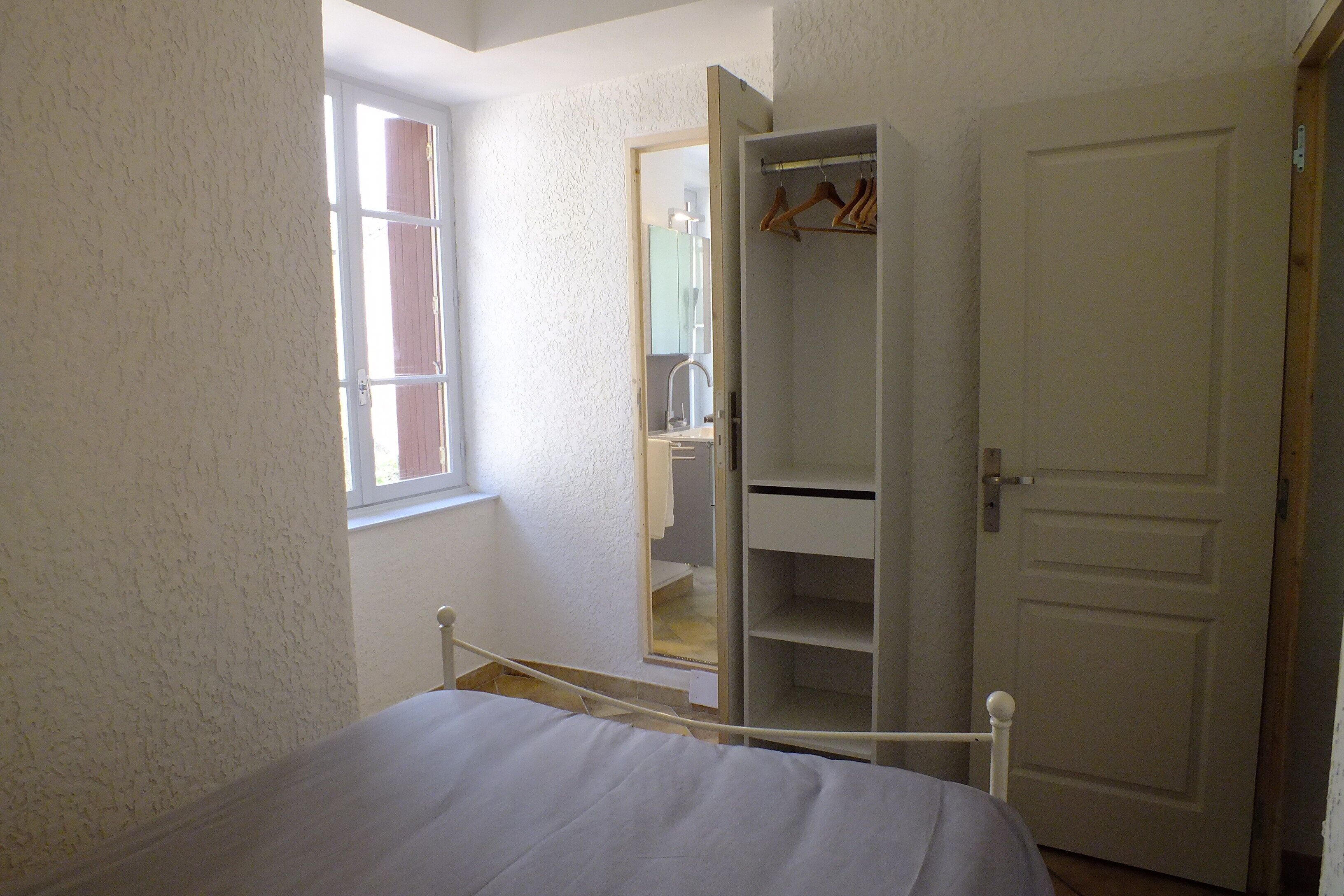 Une chambre à coucher avec un lit, une armoire, un miroir et une fenêtre.