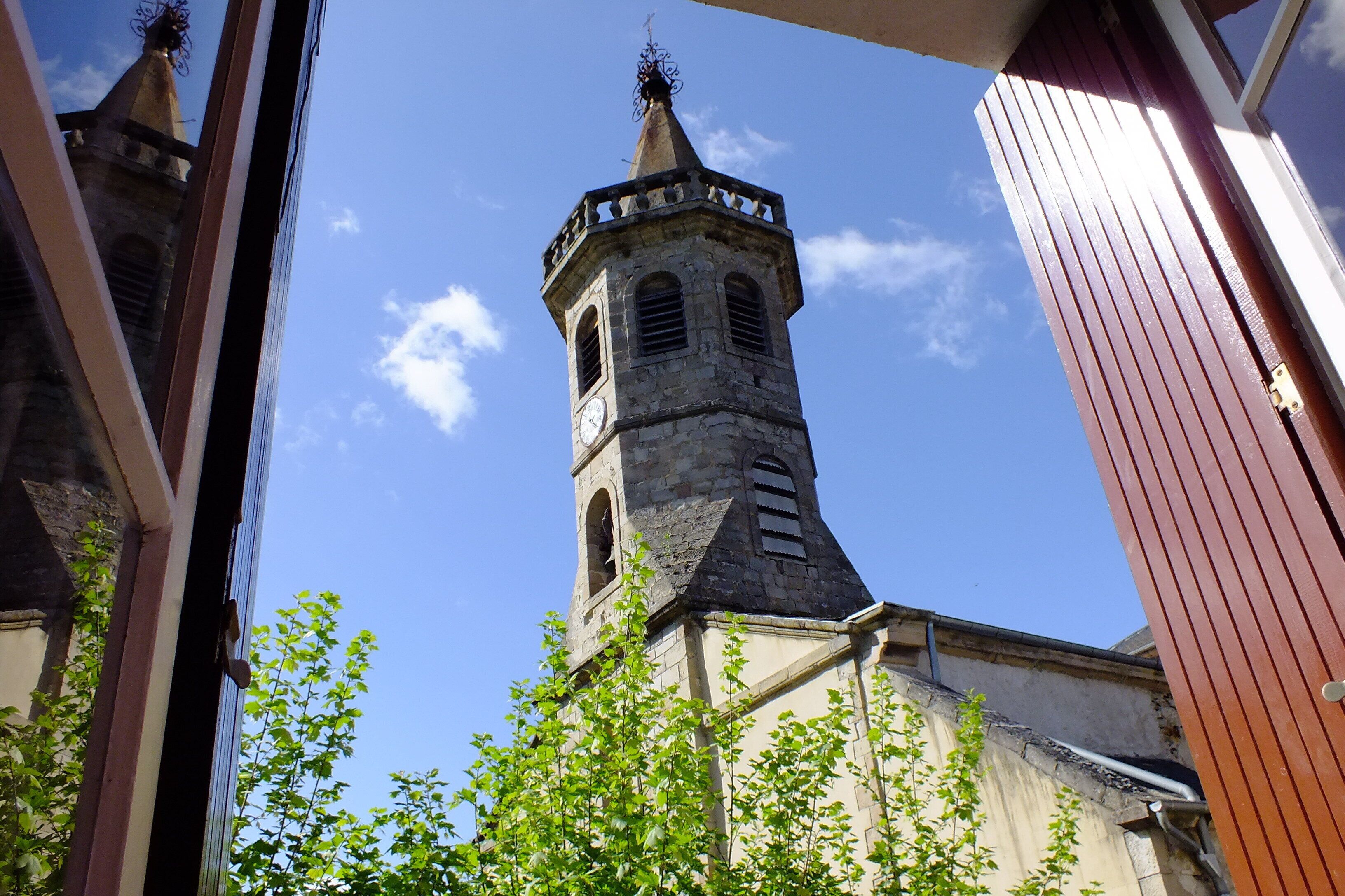 Una torre de iglesia de piedra con un reloj, rodeada de vegetación.