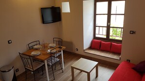 Un comedor con una mesa dispuesta para dos, un televisor montado en la pared y un rincón con cojines rojos.