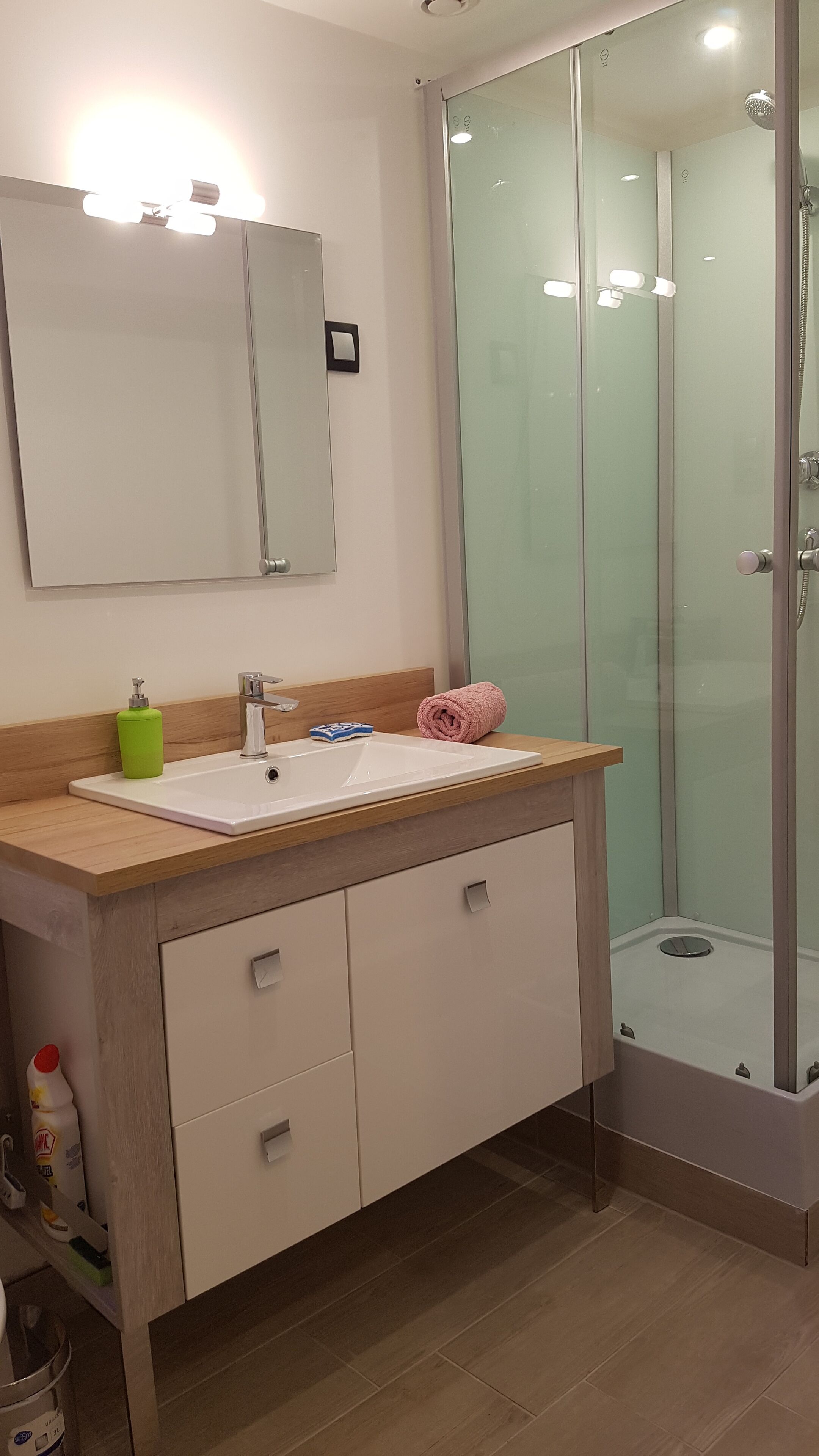 A modern bathroom with a glass shower enclosure, a wooden vanity with a sink, and a mirror above.