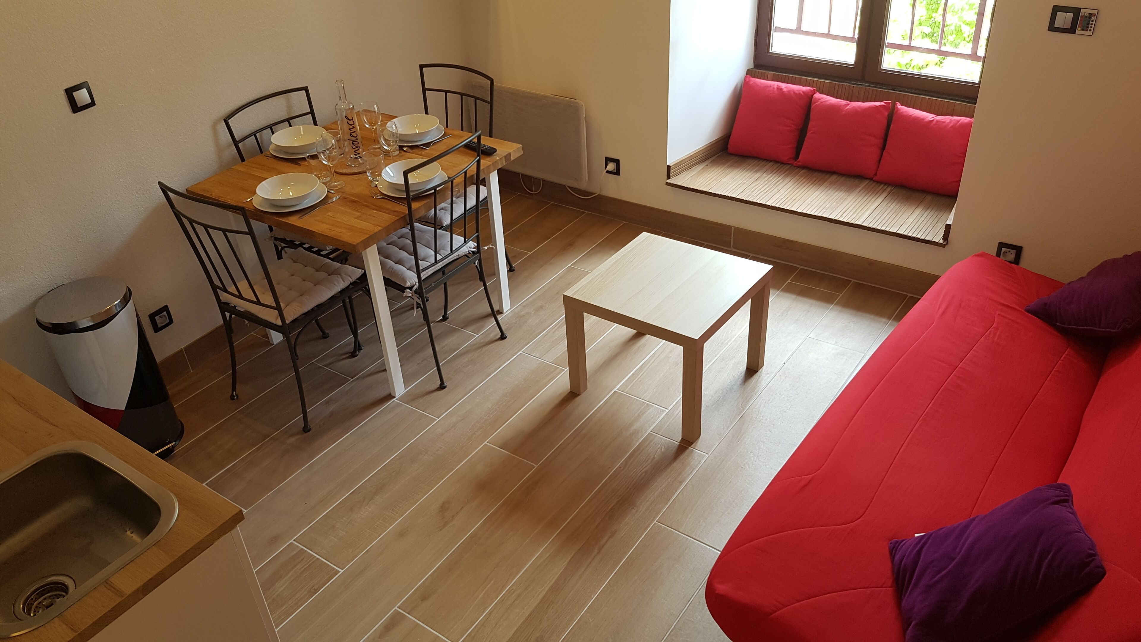 Ein Essbereich mit einem Holztisch, gedeckt für vier Personen, umgeben von Stühlen. Ein rotes Sofa und ein kleiner Tisch befinden sich im Vordergrund.