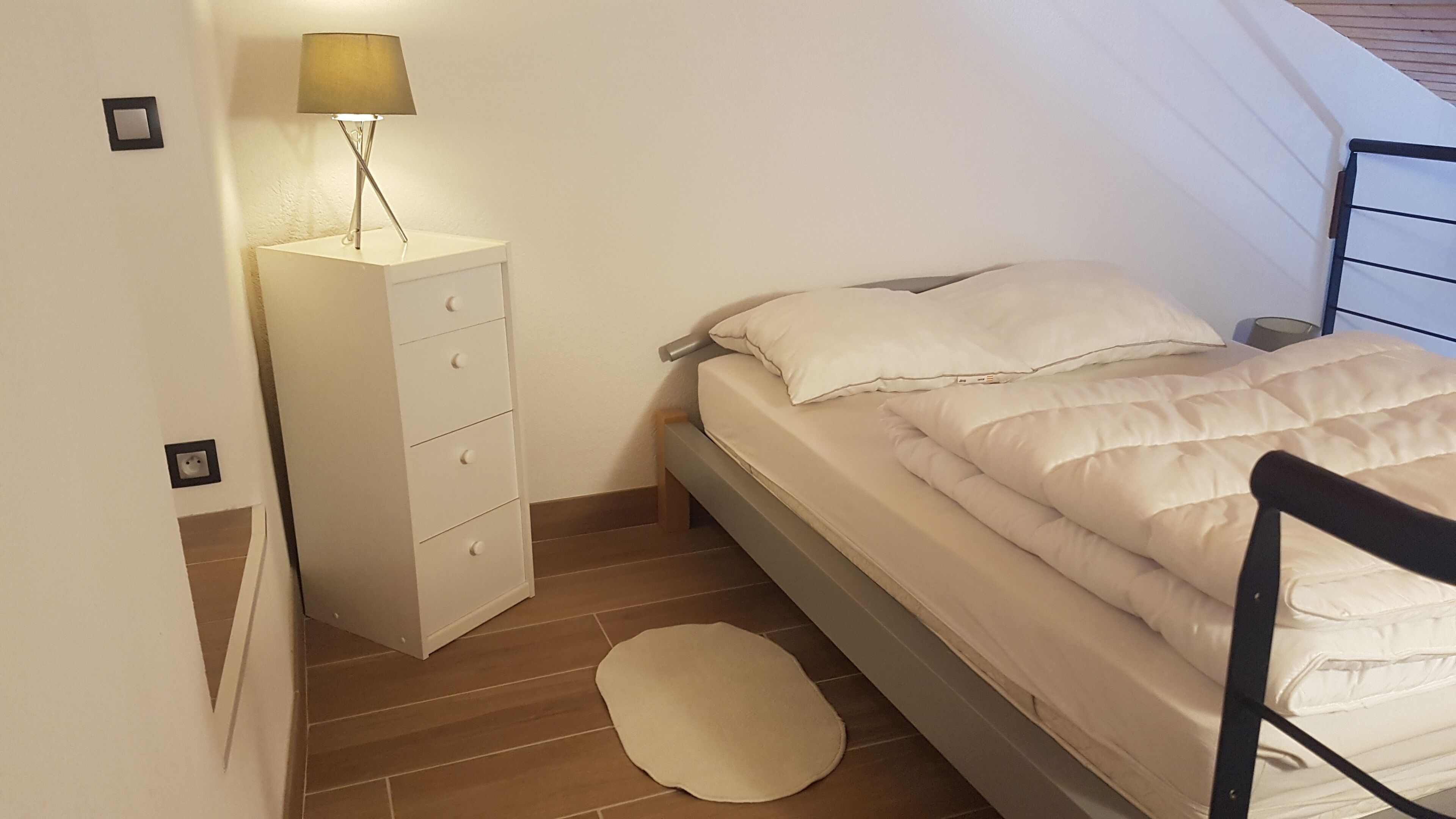 Una camera da letto con un letto, un comodino con una lampada, una cassettiera e un piccolo tappeto.