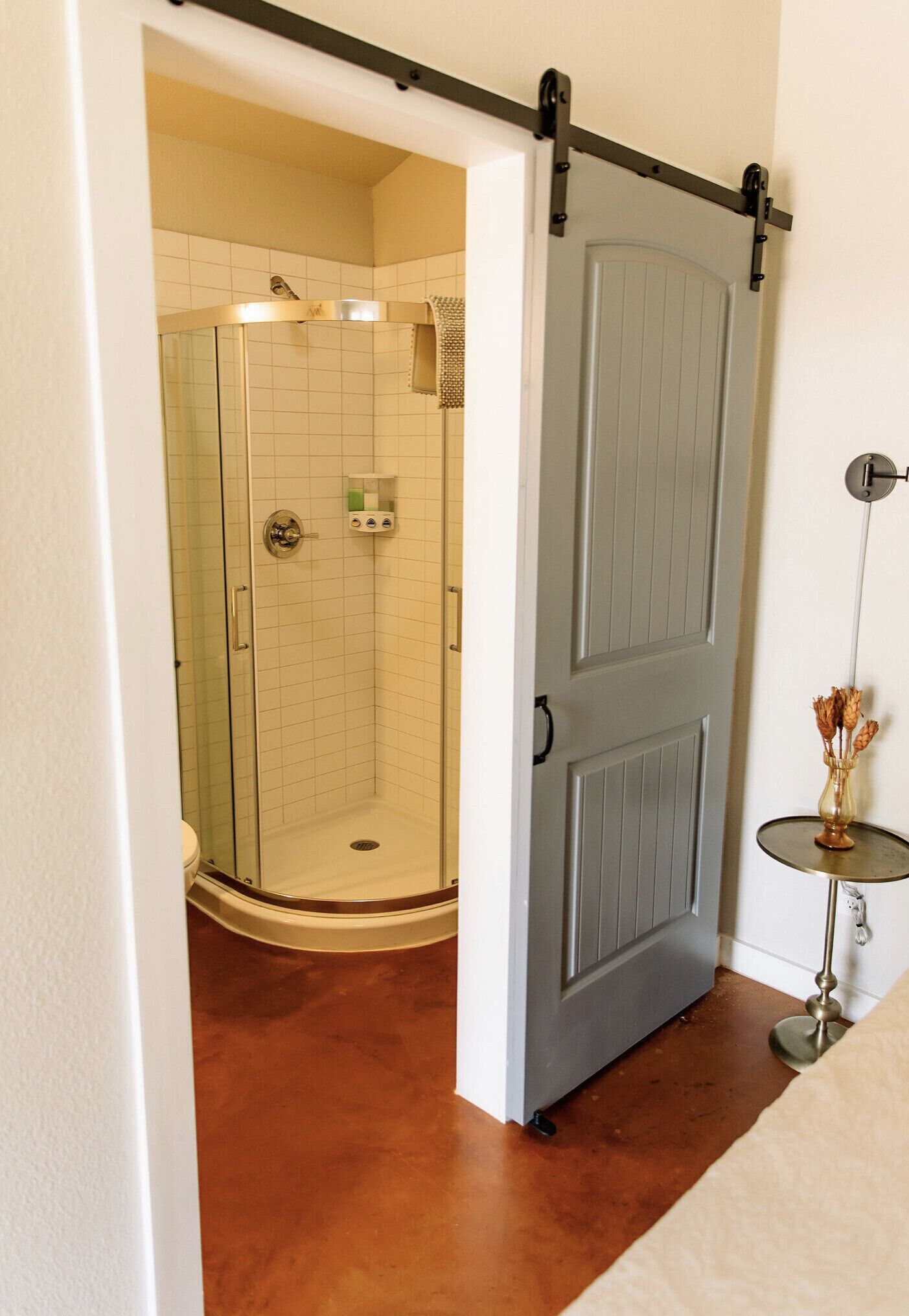 Une salle de bain avec une douche à parois de verre, une porte blanche et une petite table sur laquelle est posé un vase.