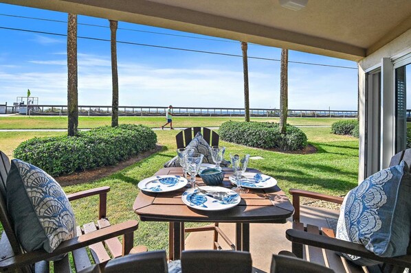 Un patio con una mesa lista para dos personas, con vista a un área verde y al mar, además de un puente.