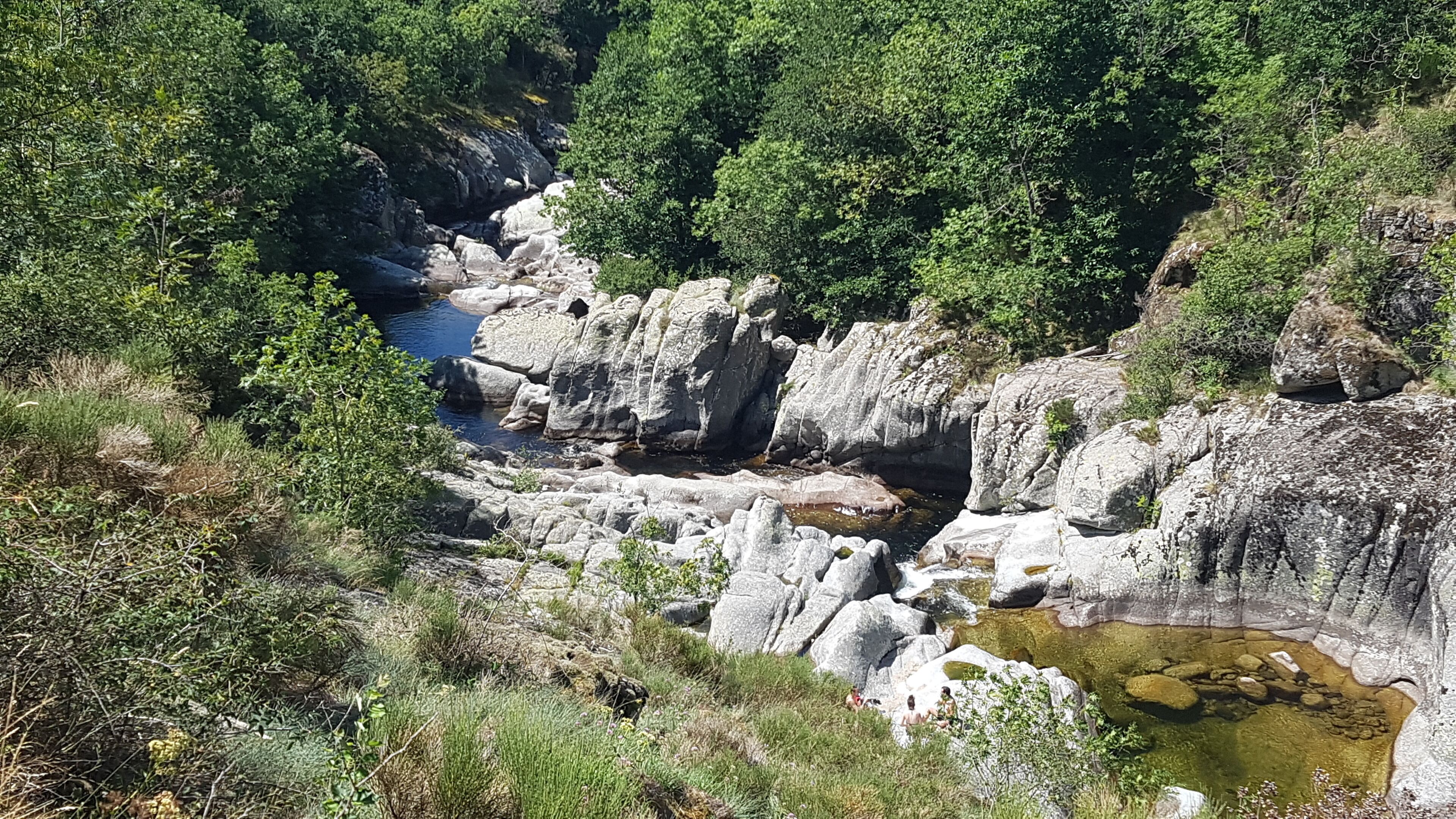 A rocky landscape with a river, dense greenery, and a small waterfall.