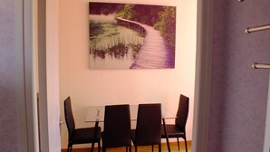 Ein Essbereich mit einem Tisch und vier Stühlen, ein Bild einer Brücke über Wasser an der Wand und eine Tür mit einem Metallgriff.