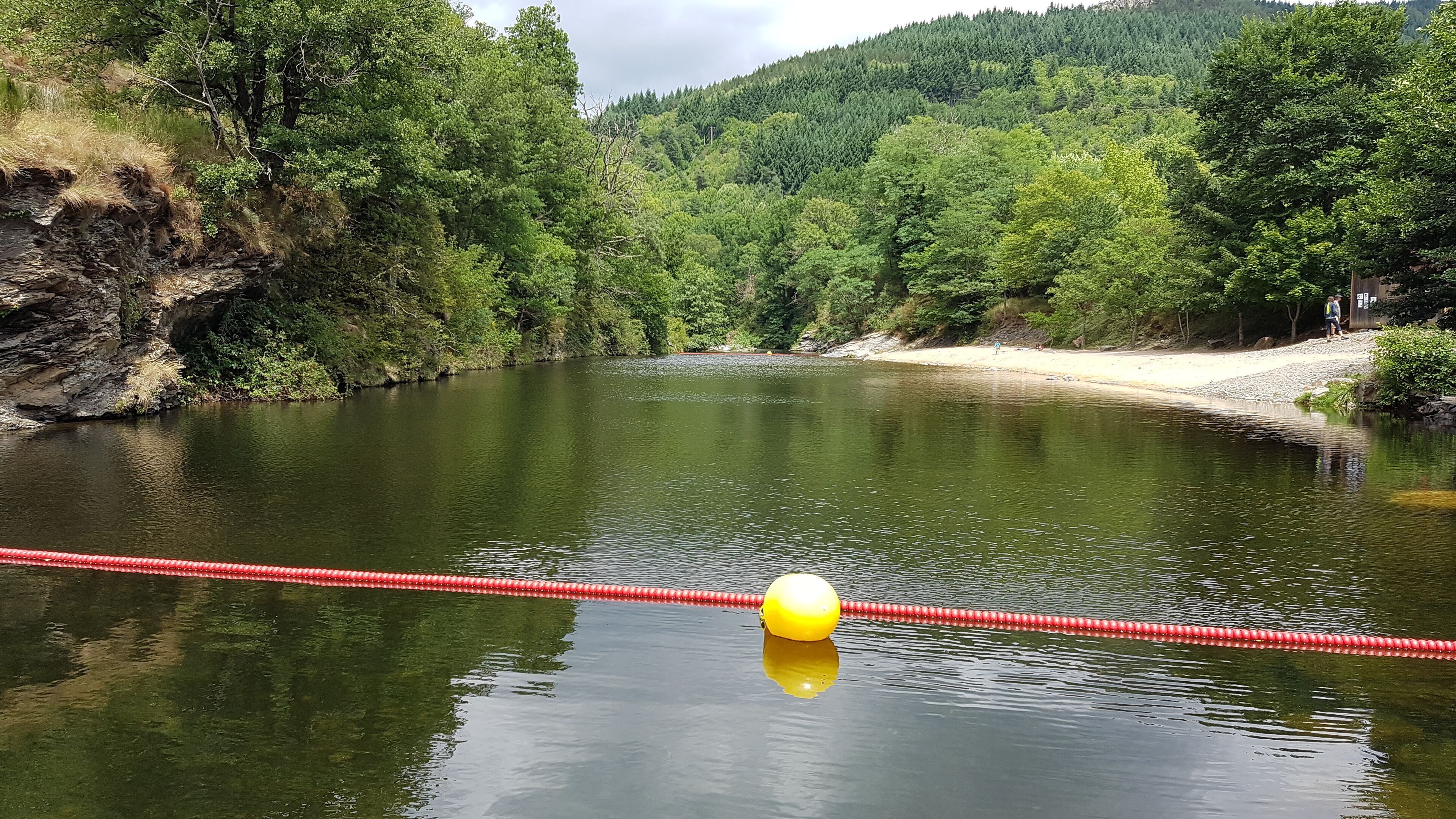 A calm river with a red rope barrier and a yellow buoy in the foreground.