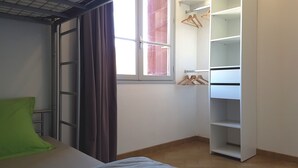 Una camera da letto con un letto, una finestra con tende, un armadio e un cuscino verde.