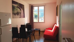 Una stanza compatta con zona pranzo, un divano rosso, una finestra vista verde e un frigorifero.