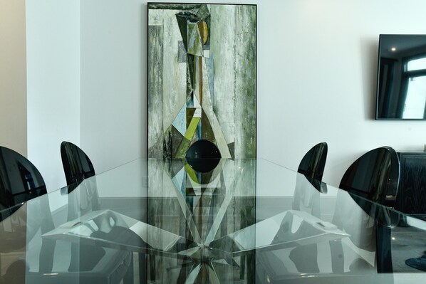 Une salle de conférence avec une table en verre et des chaises noires, un grand tableau abstrait accroché au mur et un téléviseur à écran plat fixé au mur.
