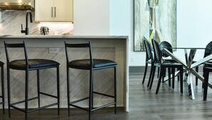 Une cuisine moderne dotée d’un plan de travail en marbre, de deux tabourets de bar noirs et d’un coin repas avec une table et des chaises en verre.