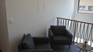 A modern living room with a sofa and armchair, a small round table, and a balcony railing. - Weingut Bugner Meizelhof (Klein-Winternheim)